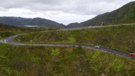 Cars-driving-on-serpentine-road-above-Lagoa-di-Fogo-lake,-flyover-view
