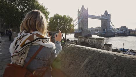Attractive-Blonde-female-traveler-taking-pictures-of-London-Tower-Bridge,-back-view