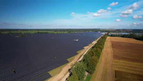 Aerial-view-descending-to-border-of-agricultural-farmland-and-huge-solar-panel-array-generating-clean-green-renewable-energy