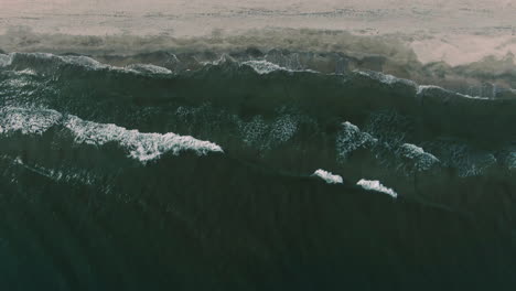 Ascending-drone-shot-over-the-seashore,-with-mesmerizing-waves,-on-a-clear-sunny-day