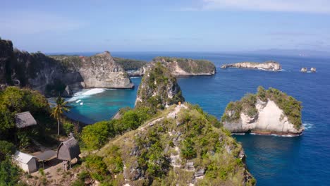 Distant-aerial-view-of-a-person-walking-along-the-top-of-a-cliff-on-the-tropical-island-of-Nusa-Penida,-Indonesia