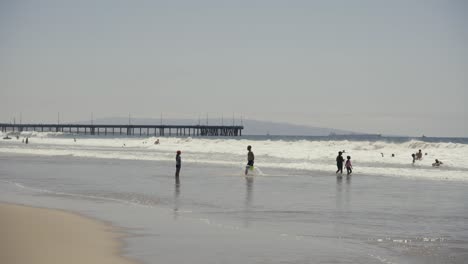 Personas-Y-Familias-Nadando-Y-Caminando-En-La-Playa-De-Venecia-Con-Un-Muelle-Al-Fondo-Por-La-Tarde