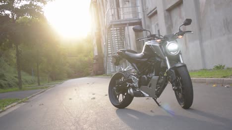 Pan-shot-of-a-motorcycle-with-led-light-in-front-of-a-industrial-building-and-sunset-in-the-backgorund