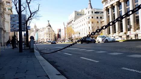 Low-angle-slow-motion-shot-of-Madrid-Intersection,-Traffic-on-Calle-de-Alcalá-with-the-famous-Edificio-Metropólis-building-and-Gran-Via-in-the-background