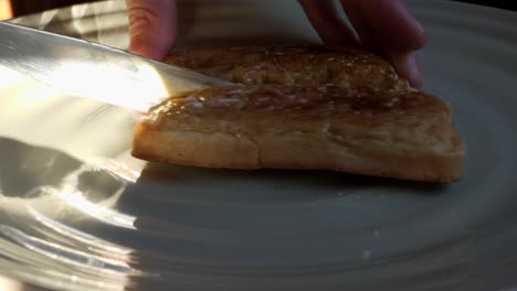 Male-hand-cutting-buttered-crumpet-in-half-on-plate