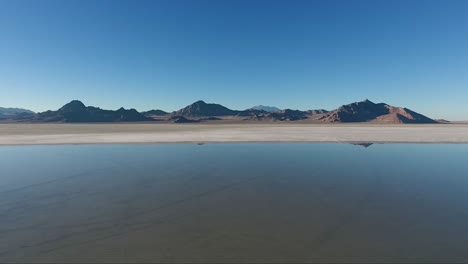 An-aerial-drone-shot-reveals-smooth-water-covering-the-white-salt-of-the-Bonneville-Salt-Flats-and-distant-mountains