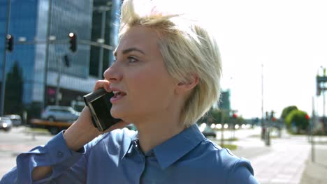 Young-beautiful-woman-with-blonde-hair-and-green-eyes-wearing-a-blue-button-up-top-in-city-on-phone-anxiously-receiving-bad-news-and-having-a-conversation