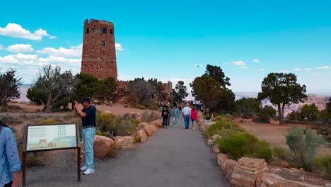 Walking-shot-towards-Grand-Canyon-and-Desert-View-Watchtower-with-tourists-in-Grand-Canyon-National-Park,-Arizona,-USA