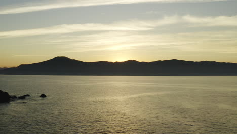 Schöne-Luftdrohnenansicht-Sonnenuntergang-Goldene-Warme-Farben-über-Dem-Meer-Und-Bergen-Am-Horizont