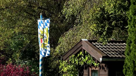 Bavarian-flag-waving-in-the-wind-in-front-of-a-summerhouse,-Germany