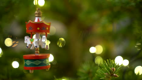 Rotierendes-Holzkarussell-Mit-Weißen-Pferden-Als-Weihnachtsbaumdekor,-Das-Im-Dezember-An-Der-Tanne-Mit-Verschwommenen-Lichtern-Im-Hintergrund-Hängt