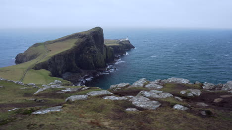Tracking-shot-of-Neist-Point-lighthouse-with-rocky-cliffs-in-foreground-and-Atlantic-Ocean-in-the-background-on-a-windy-and-cloudy-day-in-Scotland,-Isle-of-Skye