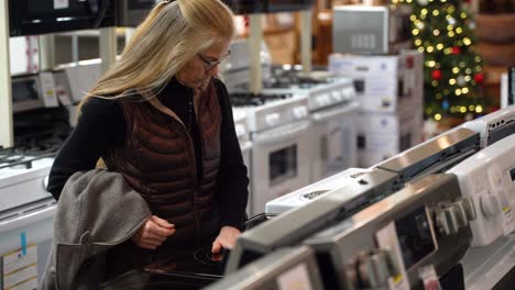 Closeup-of-pretty-mature-blonde-woman-shopping-for-a-stove-at-a-kitchen-appliance-store-showroom