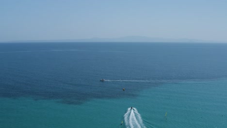 Aerial-drone-shot-backwards-of-boat-and-jet-ski-in-clear-blue-sea