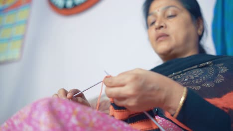 Footage-from-below-of-Indian-woman-knitting-a-scarf-with-red-and-black-wool-and-two-needle-crafts