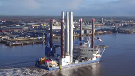 Sea-Challenger-vessel-under-sail-past-docks-with-wind-turbine-blades-and-towers-onboard