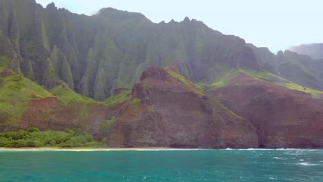 4K-Hawaii-Kauai-Boating-on-ocean-left-to-right-pan-from-waterfall-in-distance-and-mountain-shoreline-to-backlit-mountain-shoreline