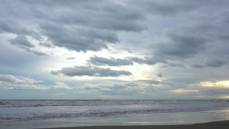Gewitterwolken-Durchziehen-Den-Himmel-Mit-Goldenen-Sonnenstrahlen-Während-Des-Sonnenuntergangs-An-Einem-Strand,-An-Dem-Das-Meer-Gegen-Den-Sand-Bricht