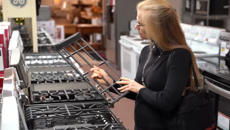 Pretty-mature-blonde-woman-looking-at-the-features-and-benefits-of-a-gas-stove-in-a-kitchen-appliance-store