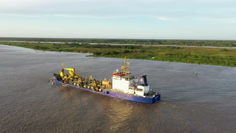 Commercial-Ship-Sailing-Out-Of-Barranquilla-Port-On-The-Magdalena-River-During-Golden-Hour-Sunset