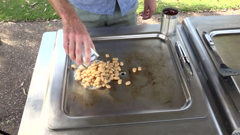 Person-pours-can-of-beans-onto-outdoor-cooking-hot-plate,-medium-shot