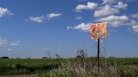 A-trashed-sign-warning-of-a-deep-channel-is-seen-on-a-rural-area-of-Santa-Fe-Province,-Argentina,-with-a-soy-sown-field-in-the-background