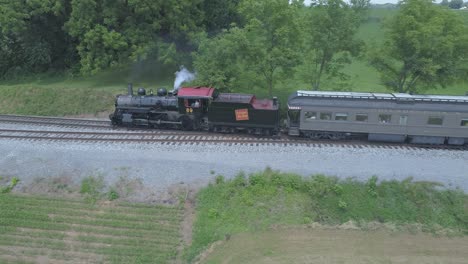 Aerial-View-of-a-1910-Steam-Engine-with-Passenger-Train-Puffing-Smoke-Traveling-Along-the-Amish-Countryside-on-a-Sunny-Summer-Day-as-Seen-by-a-Drone