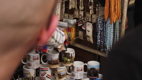 Man-picking-up-syrian-design-mugs-and-arranging-it-into-pyramid,-souvenirs-hang-on-the-background