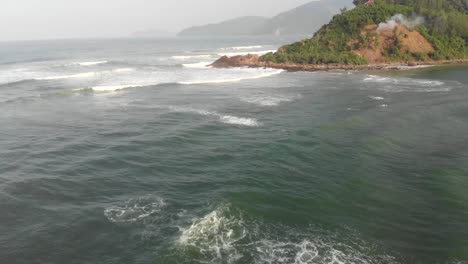 Cinematic-aerial-shot-of-small-waves-crashing-towards-small-coastal-village-at-bottom-of-hai-van-pass-mountain-road-trip-in-vietnam
