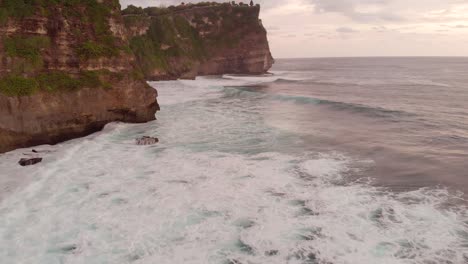 Filmische-Luftaufnahme-Eines-Lebendigen,-Wunderschönen-Sonnenuntergangs-über-Riesigen-Klippen-In-Uluwatu-Bali-Mit-Tiefblauen,-Krachenden-Wellen-Am-Fuß-Des-Ozeans-4