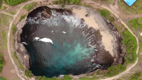 Filmische-Luftaufnahme-Der-Kreisförmigen-Felsformation-Am-Zerbrochenen-Strand-Mit-Meereswellen,-Die-An-Warmen,-Bewölkten-Tagen-Mit-Blauem-Wasser-In-Die-Mitte-Am-Rande-Der-Indonesischen-Insel-Stürzen-1