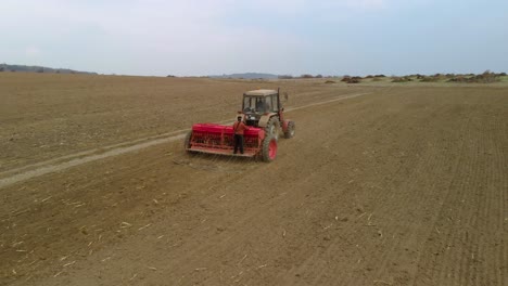 Tractor,-agricultural-machinery-and-workers-sow-a-field---aerial-tracking-shot