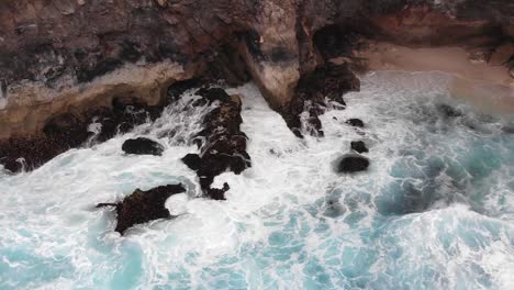 Filmische-Luftaufnahme-Der-Kreisförmigen-Felsformation-Am-Zerbrochenen-Strand-Mit-Meereswellen,-Die-An-Warmen,-Bewölkten-Tagen-Mit-Blauem-Wasser-In-Die-Mitte-Am-Rande-Der-Indonesischen-Insel-Stürzen-2