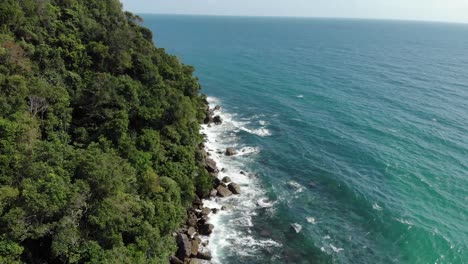 Cinematic-aerial-shot-of-clear-blue-sea-waves-crashing-against-rocky-coastline-of-forest-on-tropical-island-in-asia