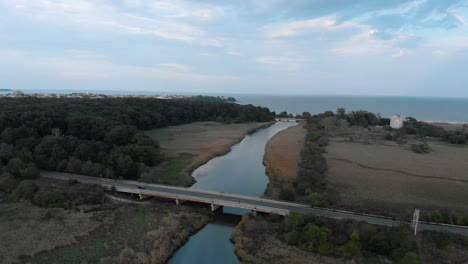 Aerial-shot-of-river-flow-into-sea-and-car-bridge-over-the-river
