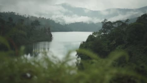 Panning-Shot-Of-The-Beautiful-Rainforest-Lake-View-With-Foggy-Mountain-On-Background