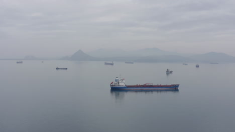 Ships-at-anchorage-waiting-area-with-mountain-ridge-in-far-distance,-on-a-calm-cloudy-overcast-day