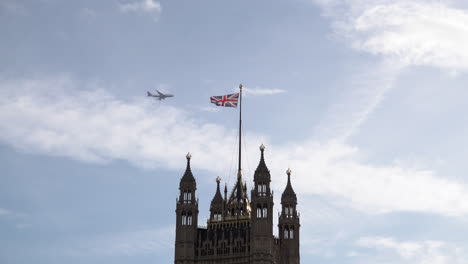 Commercial-passenger-planes-cross-a-blue-sky-and-pass-behind-Victoria-Tower-at-the-Palace-of-Westminster-in-London