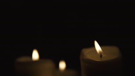 Slide-from-left-to-right,-and-take-focusing-on-burning-candles-occupy-the-whole-area,-composition-on-black-background,-take-focusing-from-blurred,-slow-motion