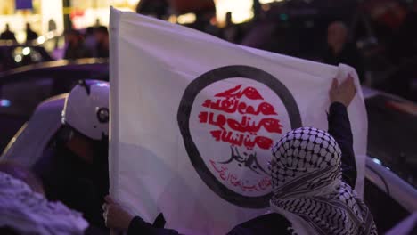 Un-Manifestante-En-Beirut,-Líbano,-Sostiene-Una-Bandera-En-Una-Calle-Concurrida,-Su-Cabeza-Está-Cubierta-Con-Una-Bufanda-Tradicional-Libanesa