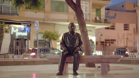 Pablo-Picasso`s-statue-in-Malaga---empty-bench-besides-it,-people-walking-in-the-background