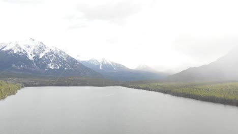 4K-footage-of-drone-flying-over-lake-in-snowy-weather-with-mountains-in-background