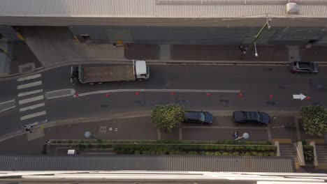 Top-down-view-of-a-small-street-with-cars,-truck,-and-people-crossing-the-road-from-the-zebra-cross