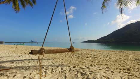 Tranquil-exotic-beach-with-white-sand-washed-by-calm-sea-on-tropical-island,-static-seesaw-hanging-from-palm-trunk-in-Malaysia