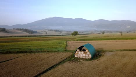Shed-with-rolls-of-hay-on-the-Tuscan-countryside-near-Florence,-Italy,-Aerial-pan-left-reveal-shot