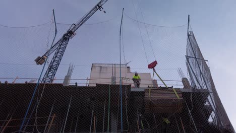 Construction-site-workers-load-building-materials-onto-crane,-Low-Angle-View