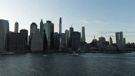 Wide-angle-aerial-view-of-Lower-Manhattan,-New-York-City-with-boats-on-the-East-River-at-dusk-on-a-clear-summer-evening