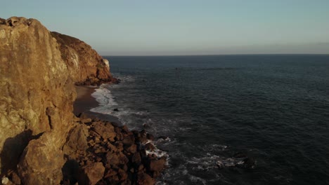 An-Aerial-Shot-of-the-Point-Dume-Cliffs-in-Malibu-in-California-as-the-Waves-Crash-Against-the-Rocks-in-the-Evening-as-the-Vibrant-Sun-Sets