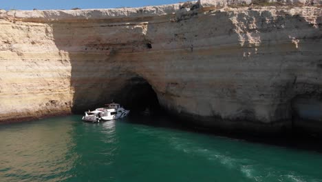Boat-cruise-exploring-caves-on-green-water-with-rocky-outcrop,-tourists