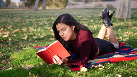 A-cute-young-woman-college-student-reading-a-book-outdoors-in-the-park-before-class-starts-in-the-fall-semester